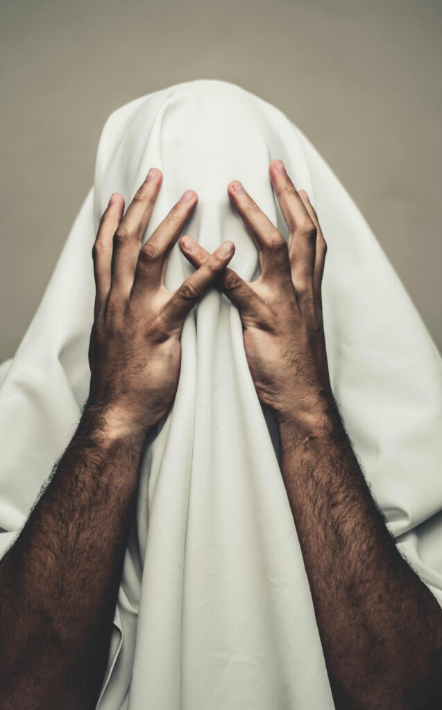 Person covered with white cloth, hands on head, expressing mystery and stress.