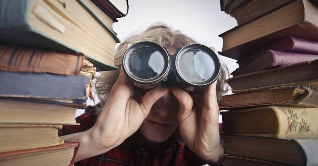 A man observing through binoculars surrounded by stacks of vintage books indoors.